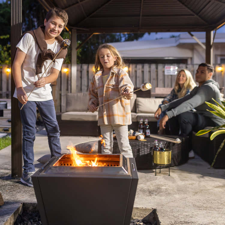 Children roasting marshmallows over a Legacy Heating fire pit during a backyard gathering.