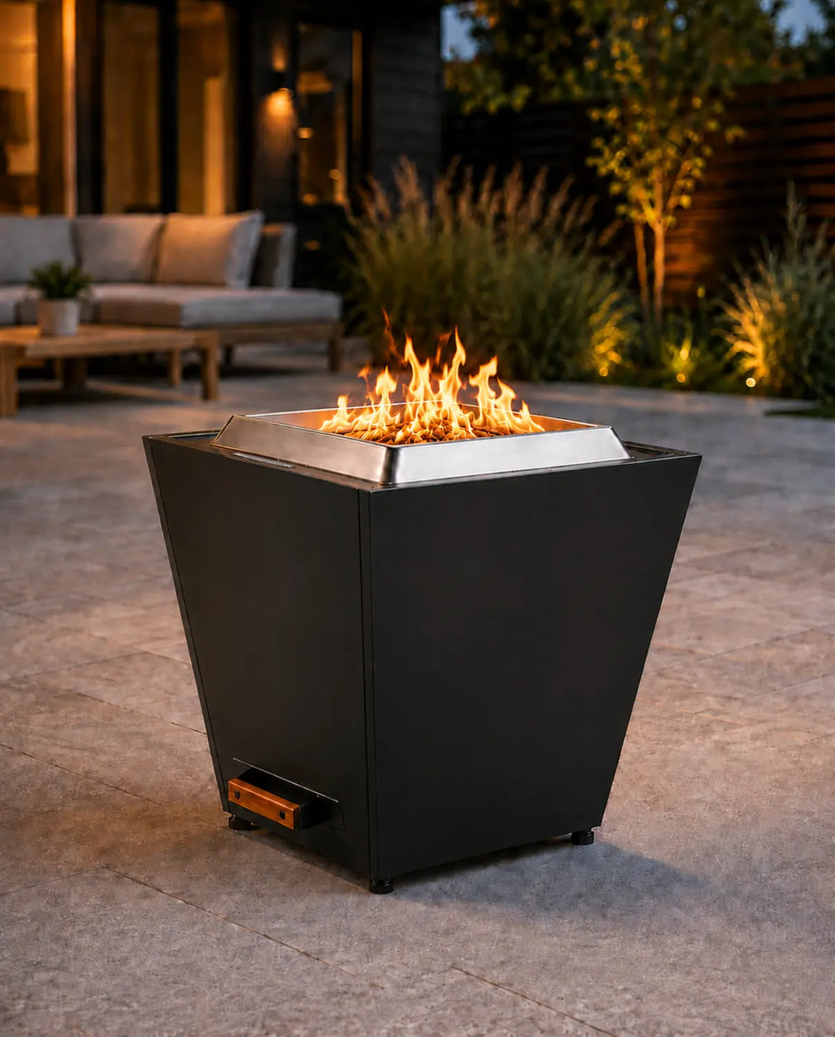 LEGACY HEATING 20-inch black flat smokeless fire pit with a four-sided tapered steel body, recessed folding handle, pull-out ash pan and natural flames on a modern backyard patio.