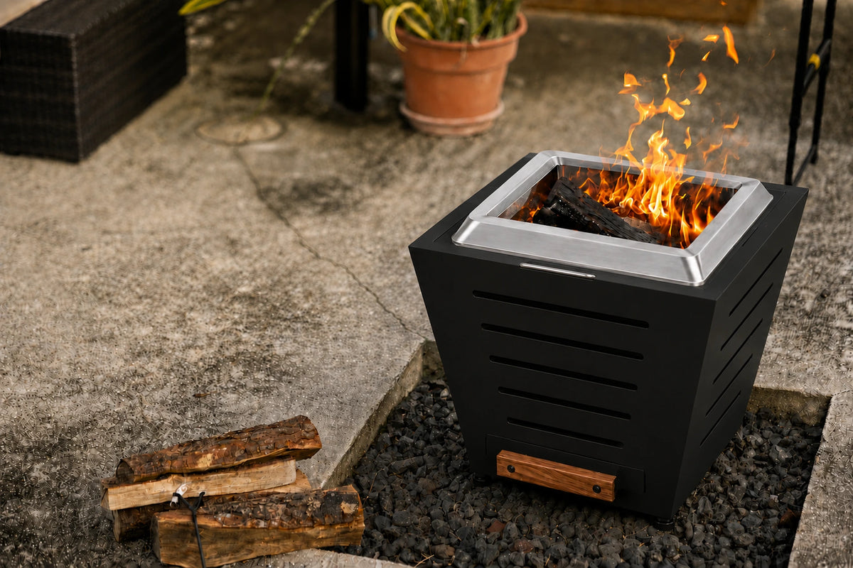LEGACY HEATING 25-inch black slatted smokeless fire pit burning on a patio, with five tapered side-panel slots, raised brushed stainless steel fire ring, a folded stainless steel handle and closed wood-handled ash pan on the same side.