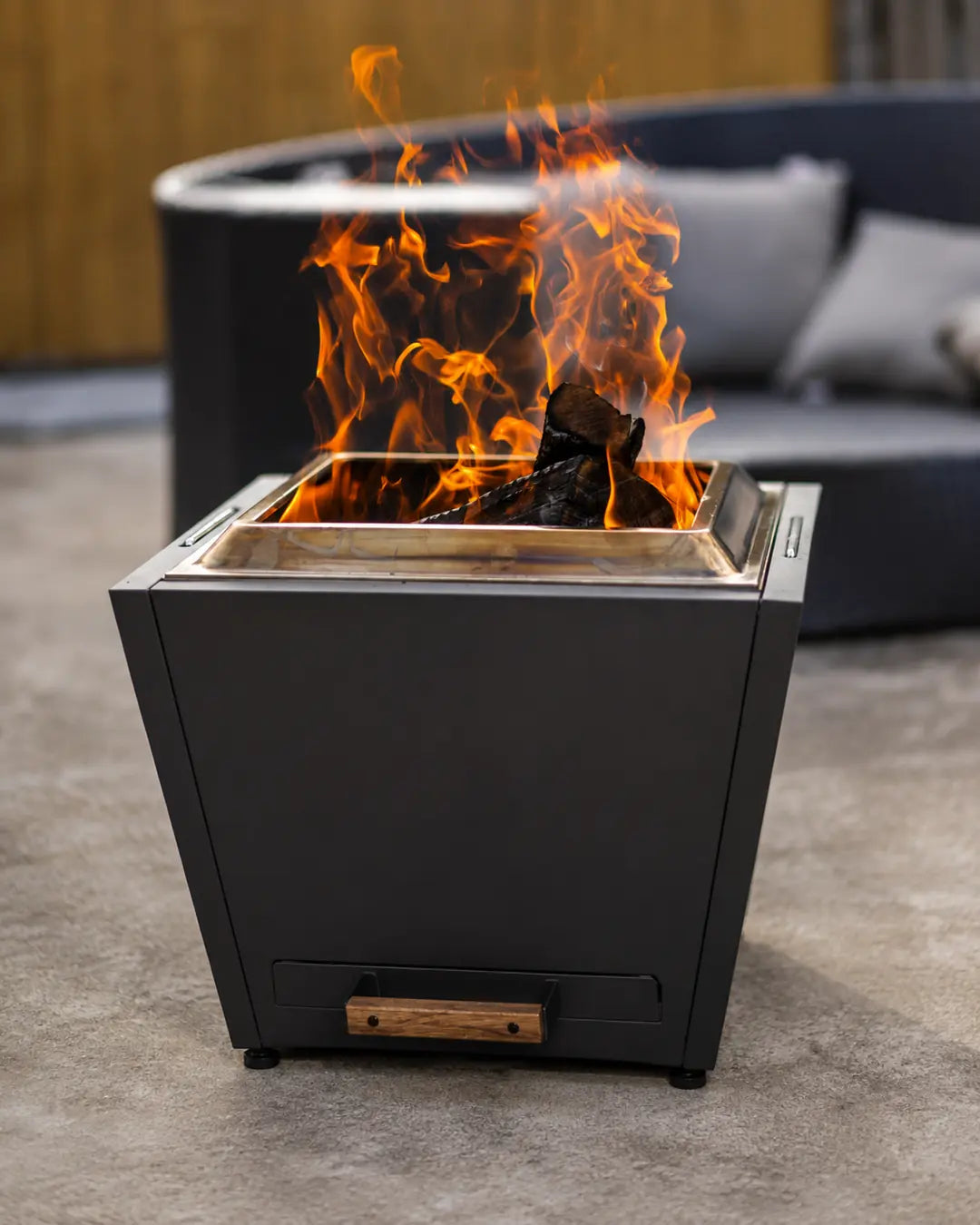 Legacy Heating 25-inch flat smokeless fire pit burning wood in a modern outdoor patio setting with a pull-out ash pan.