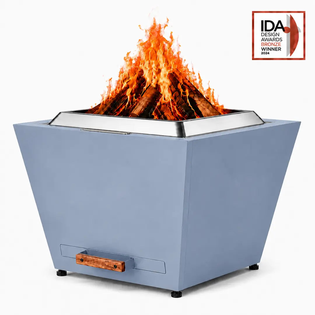 LEGACY HEATING 25 Inch Haze Blue Flat Smokeless Fire Pit with burning firewood, solid inverted-pyramid steel panels, a raised stainless steel fire ring, and a pull-out ash pan with a wooden handle.